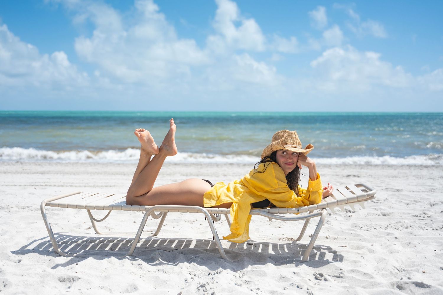 Person relaxing on a white beach lounger by the ocean shore on a sunny day.