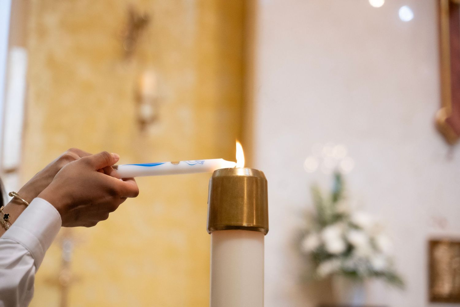 Hands lighting a large white pillar candle with a taper in a church during a religious ceremony.