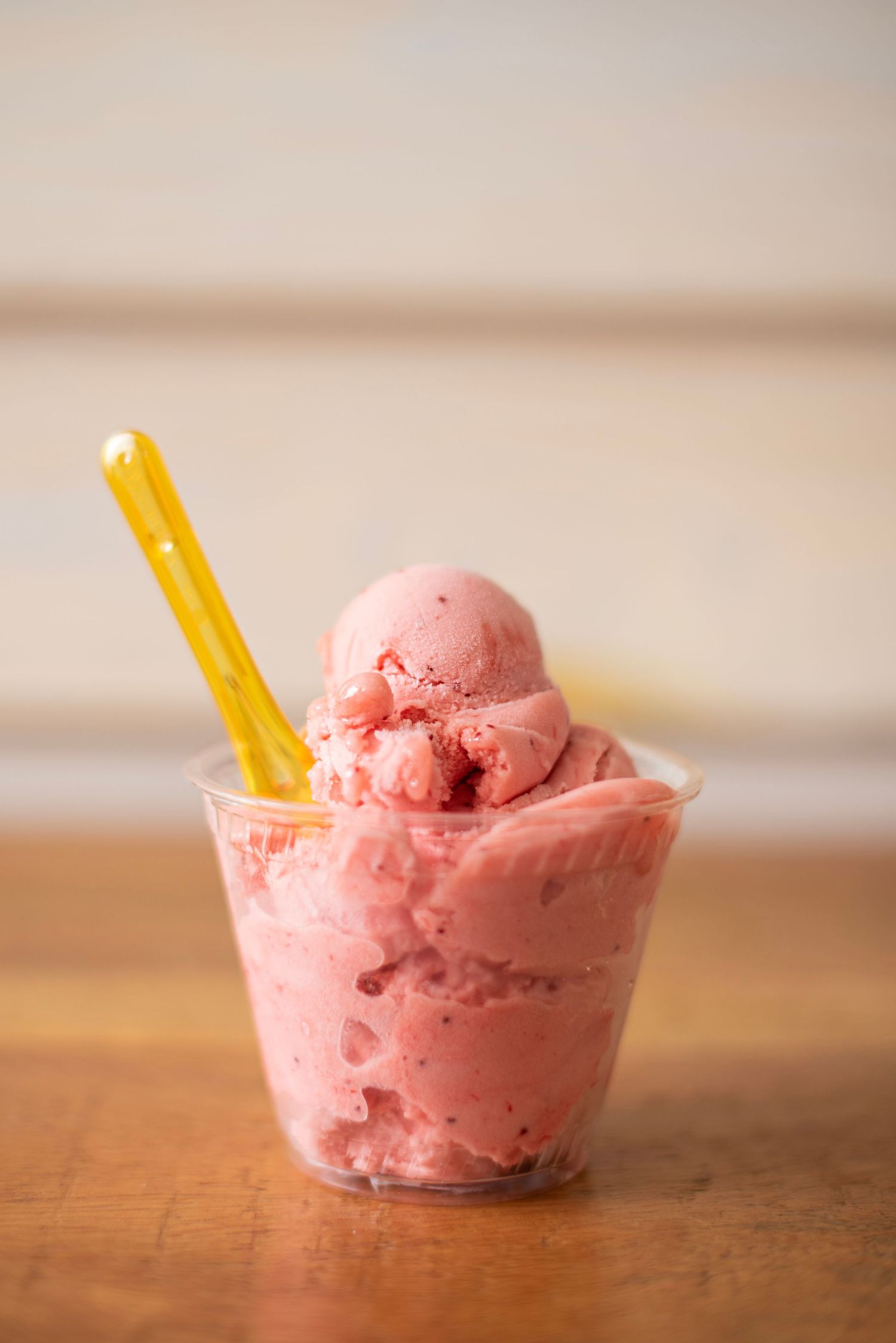 Pink strawberry ice cream scoops served in small clear bowls with yellow wafer sticks on a wooden surface.