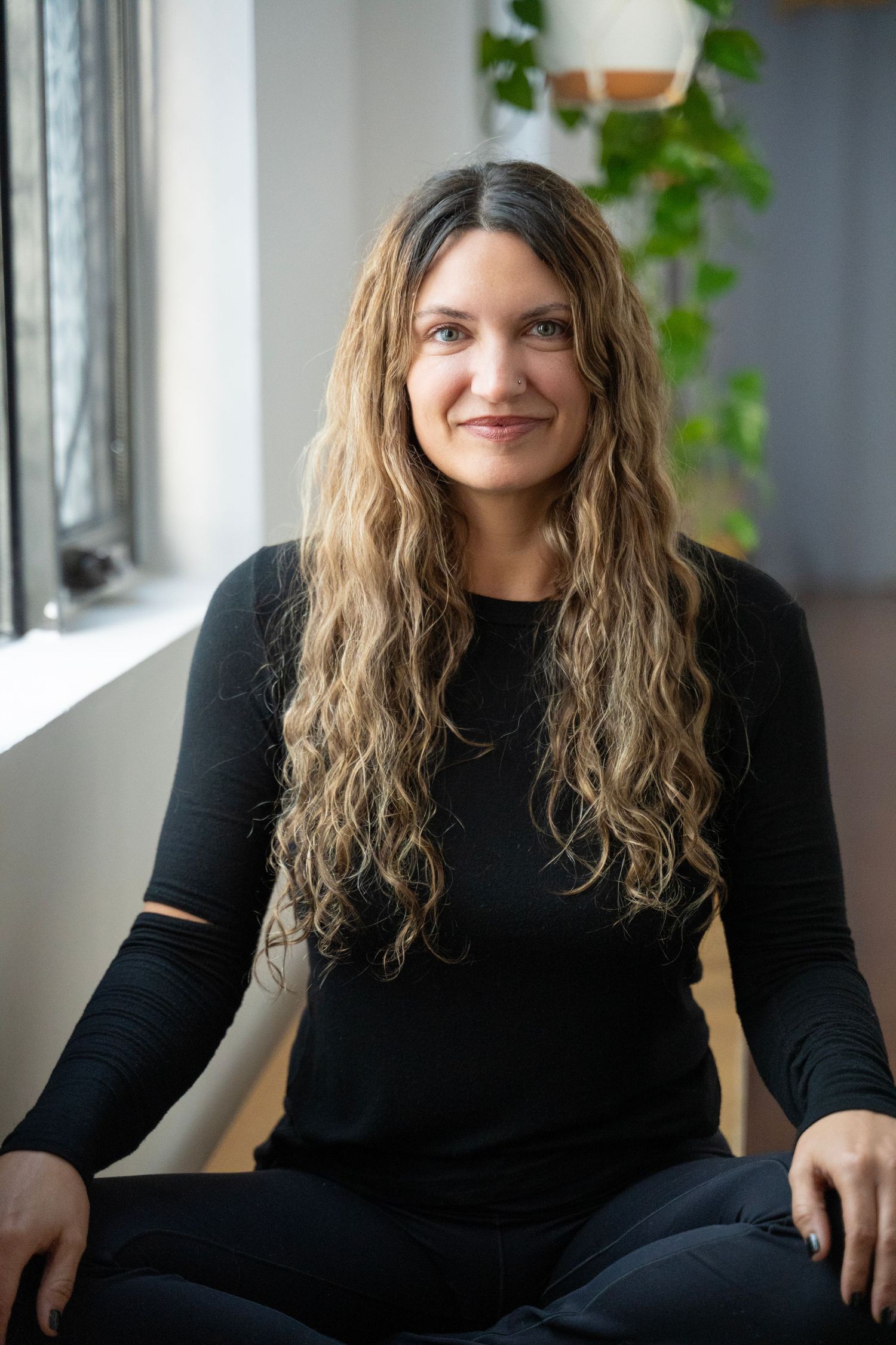 A sequence of relaxed indoor portraits featuring wavy hair and a black sweater against a bright window backdrop.