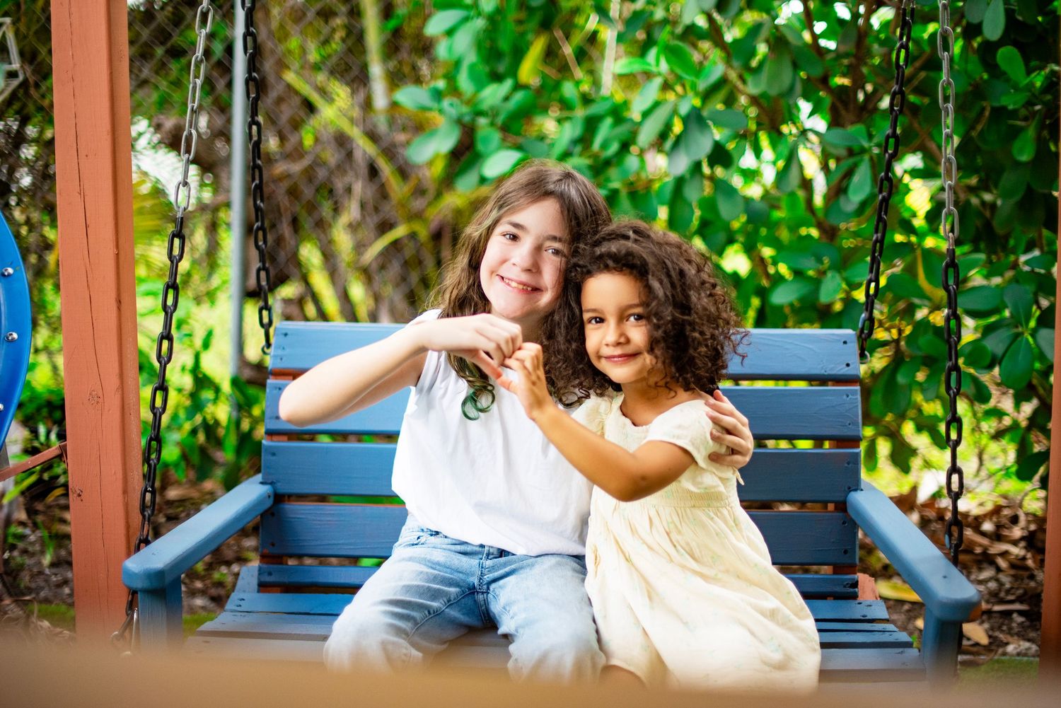 A group of people sit together on blue benches in a lush garden setting with green foliage surrounding them.