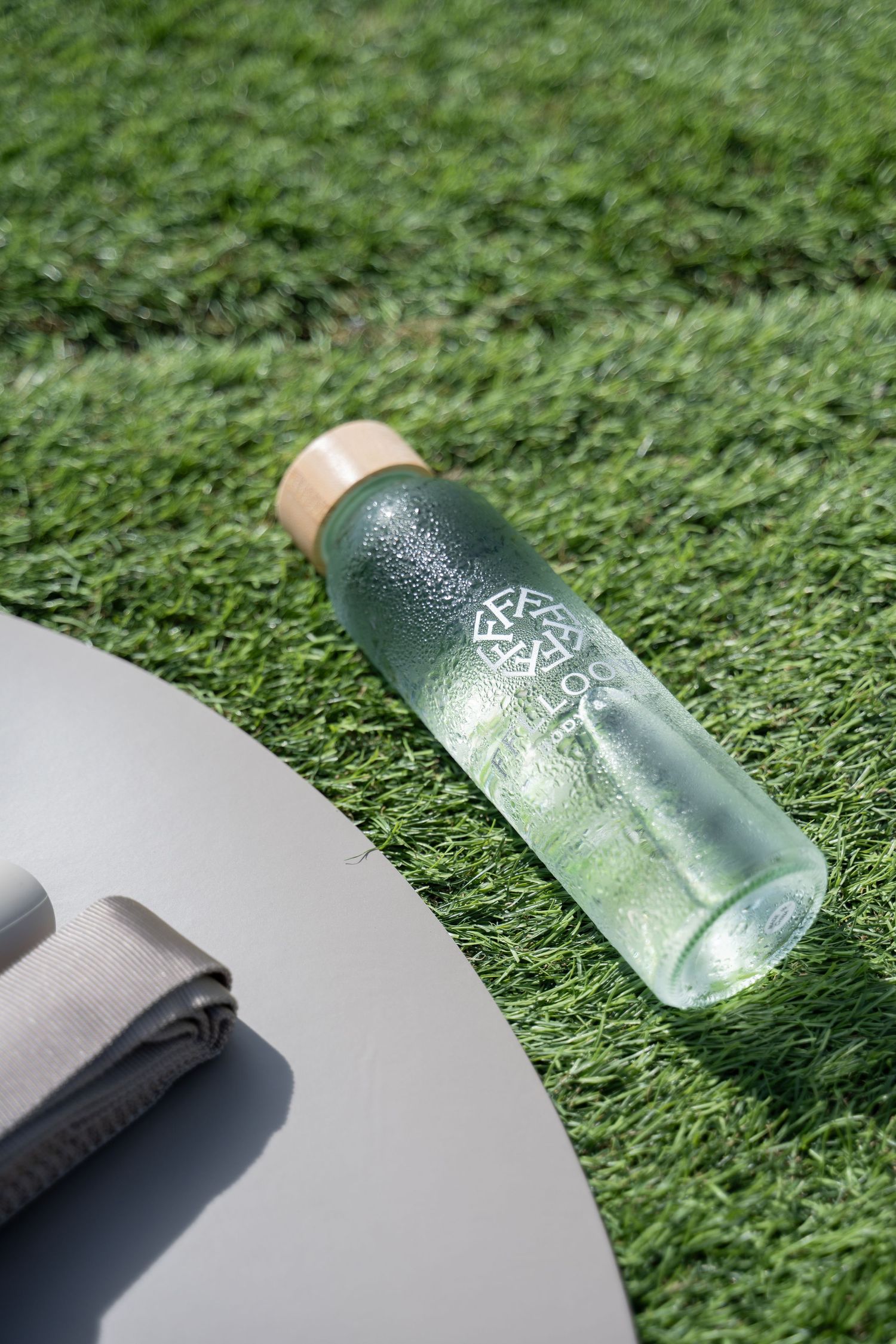 Glass bottles with condensation sitting on green grass in bright sunlight.