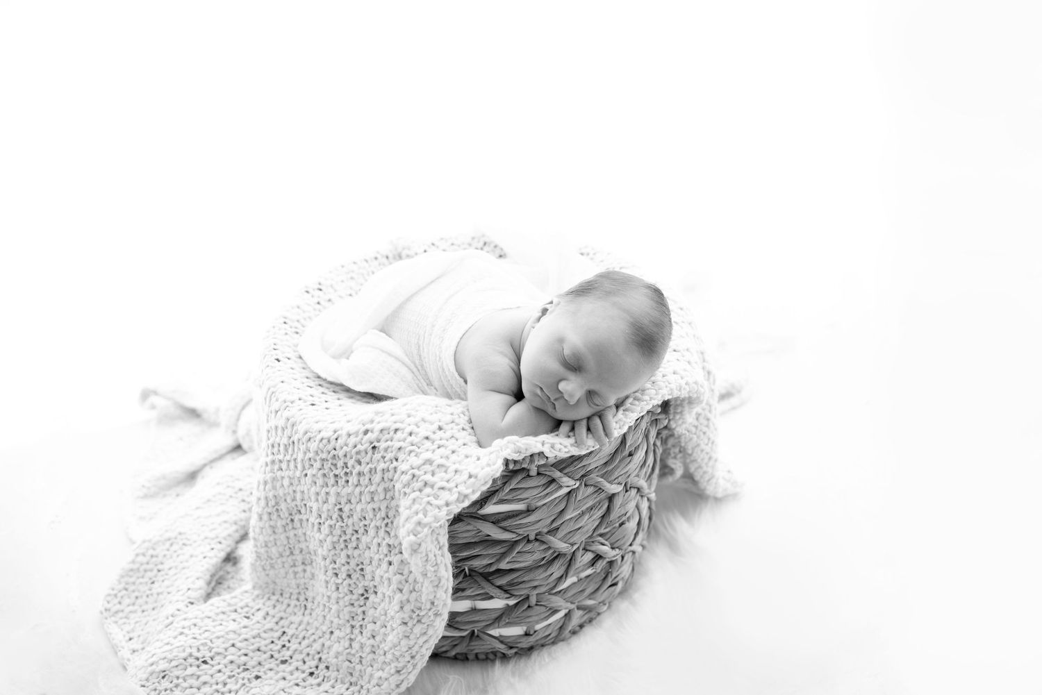 Artistic black and white portrait of a newborn resting in soft white wrapping.