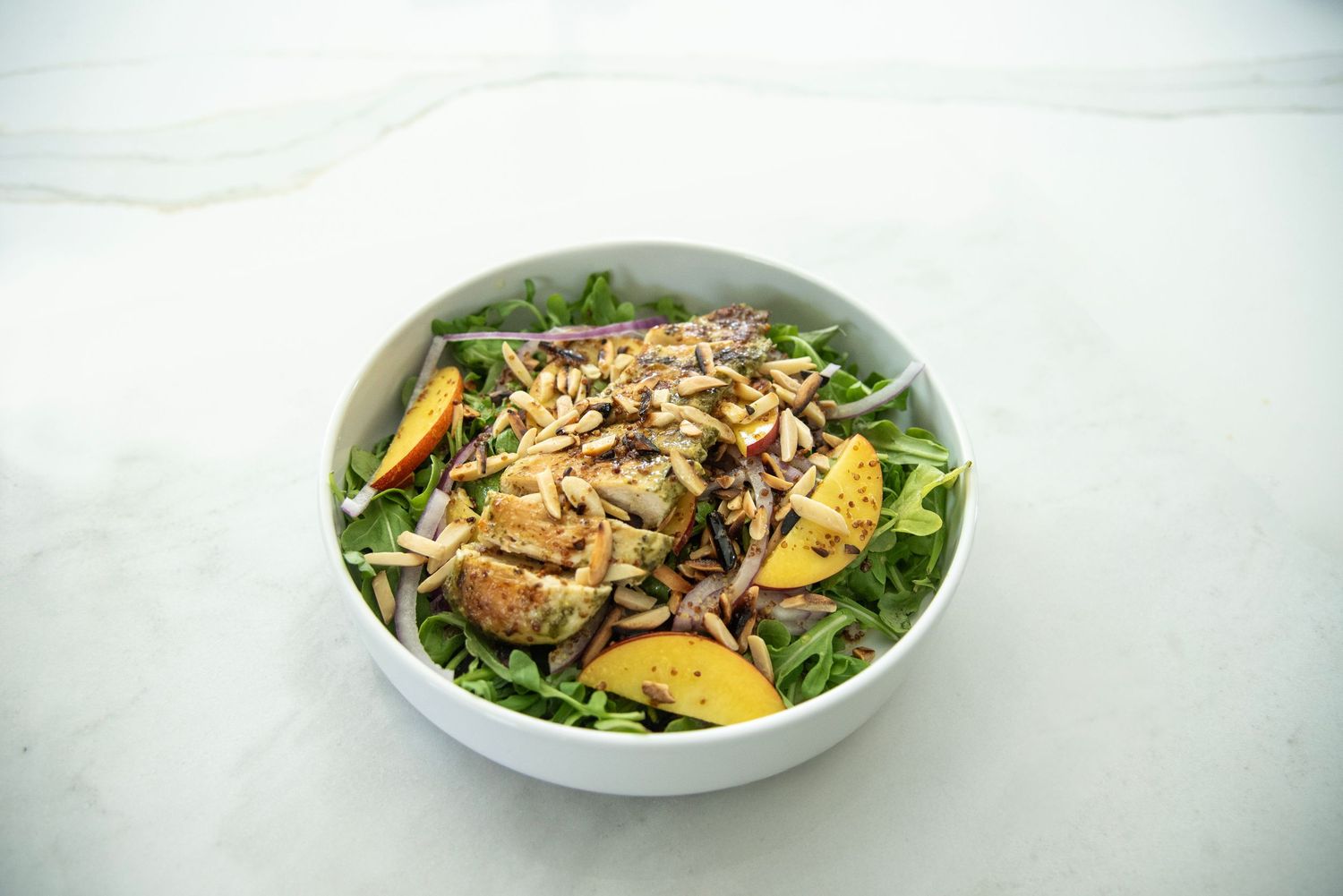 Fresh salad bowls with greens, peaches and nuts arranged in a progression sequence.