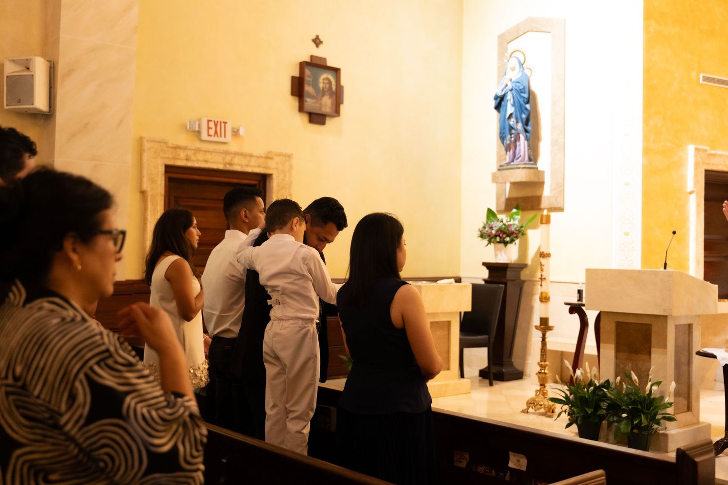 Family members stand in prayer at a Catholic church altar during a religious ceremony.