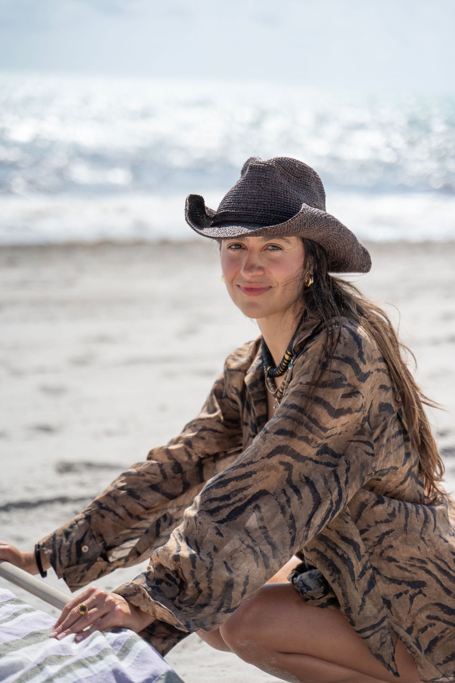 Woman in animal print jacket and baseball cap poses on beach in sequence of artistic shots.