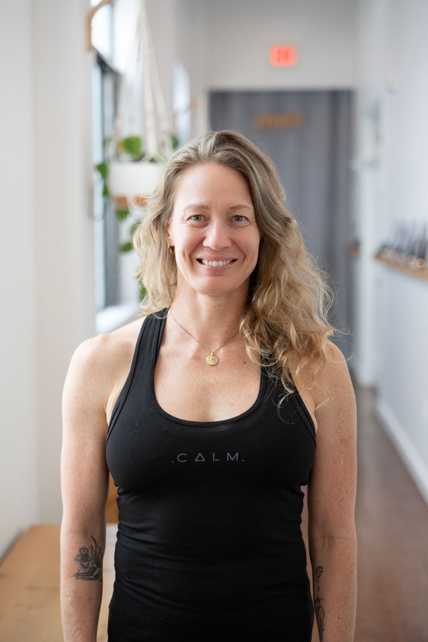 A person wearing a black tank top smiles warmly in an office hallway setting.