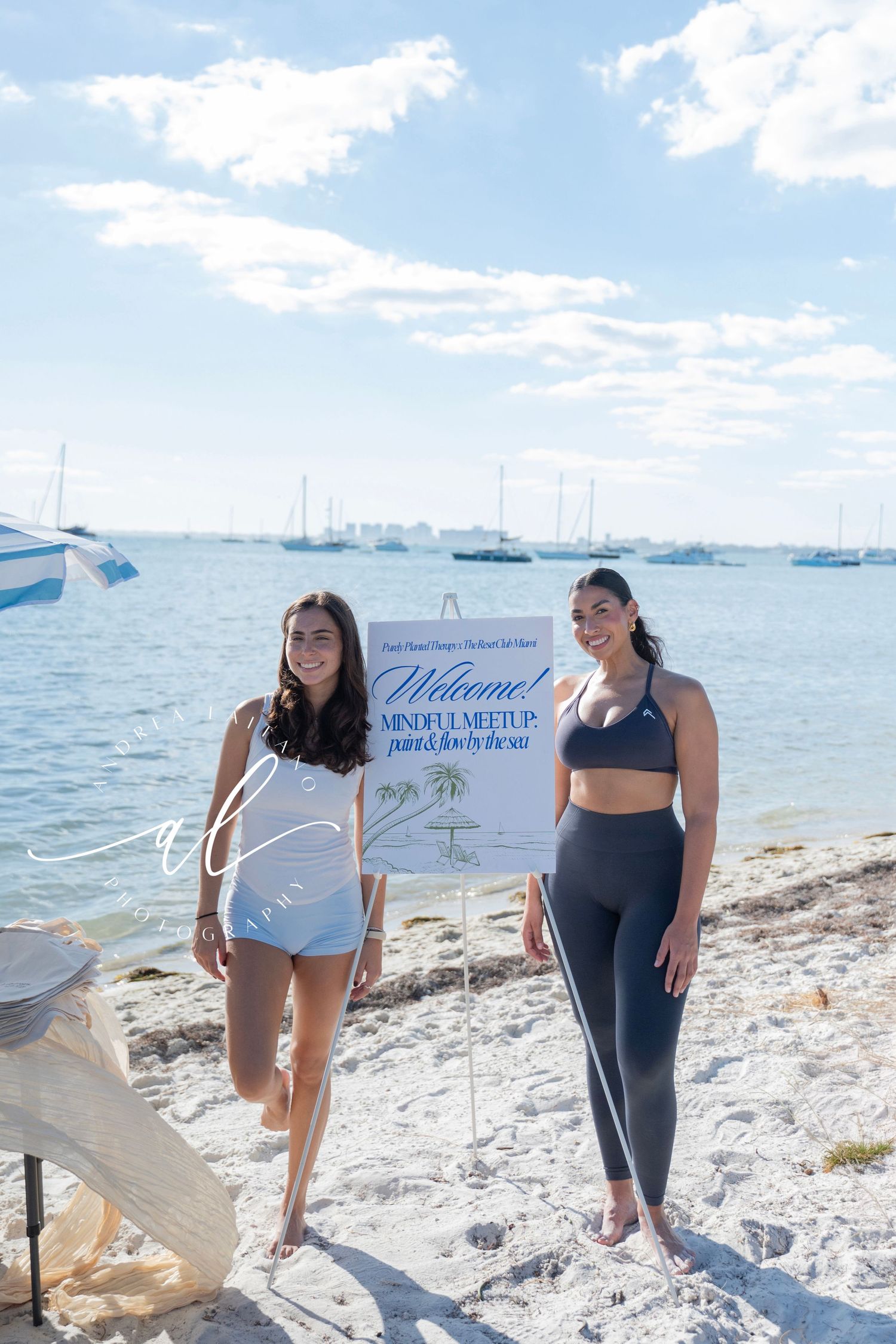 Group enjoying a sunny day at a white sandy beach with boats and yachts visible in the harbor.