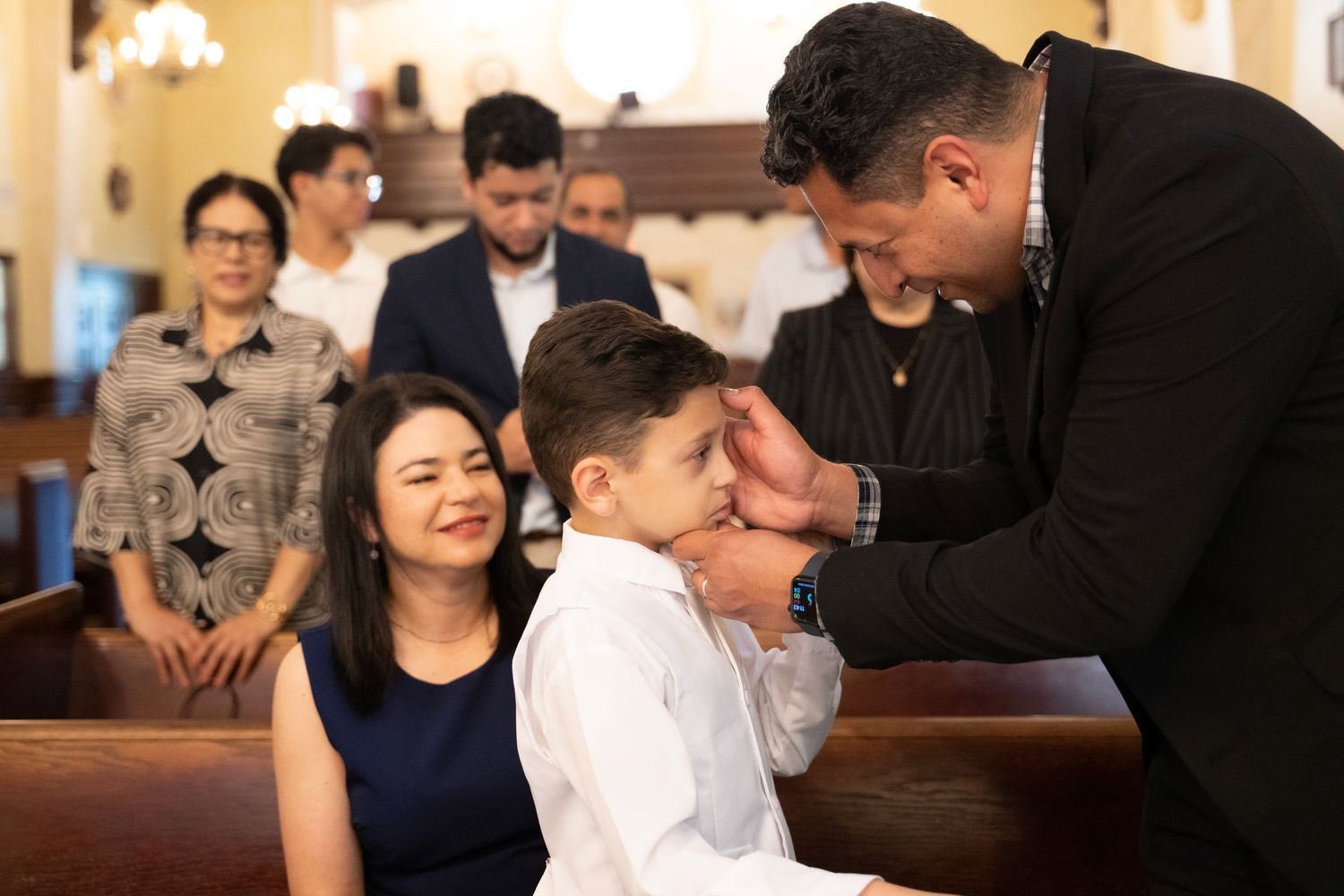 Family celebrating a child's First Communion in a church, with parents proudly smiling beside their son in white.