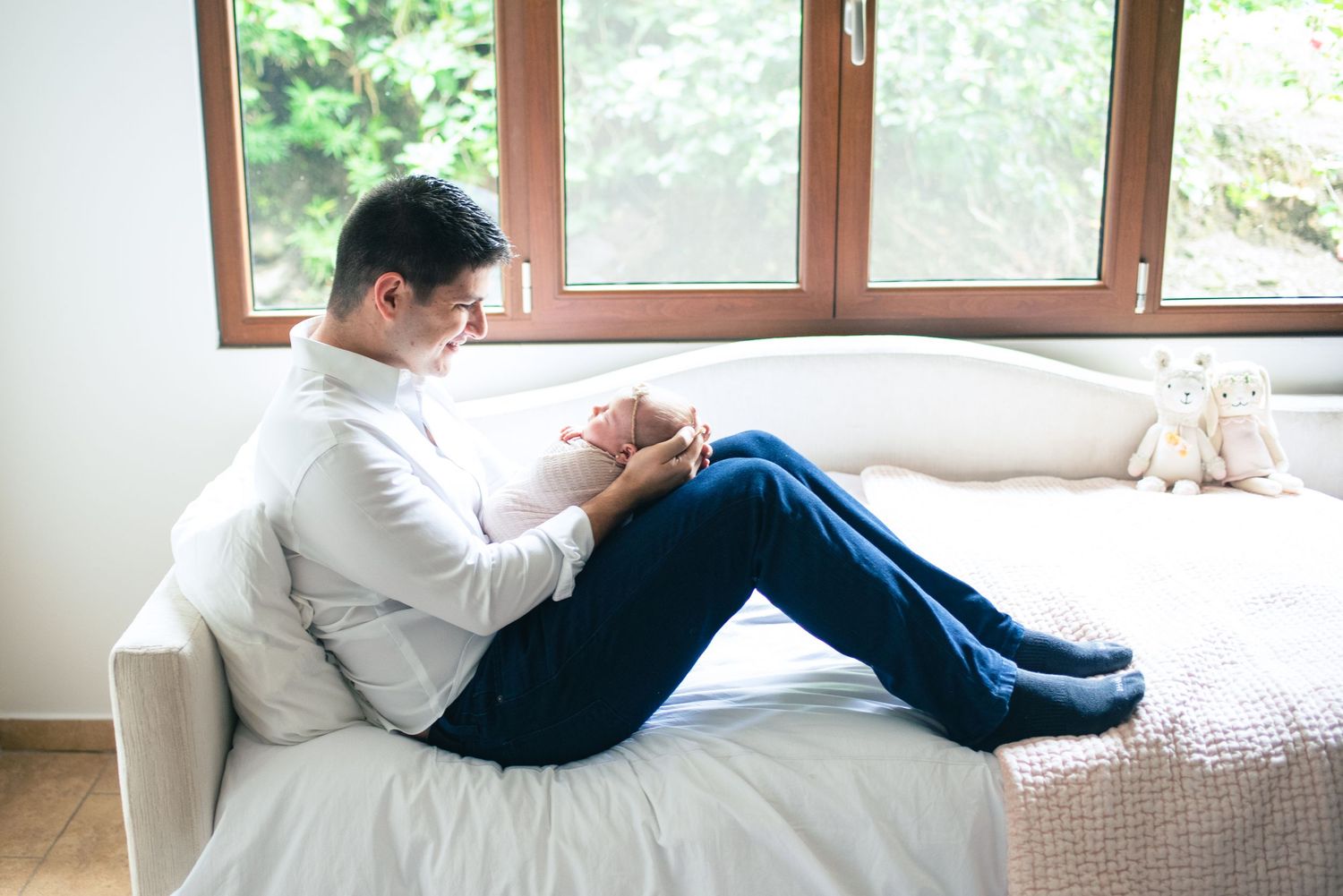A person in a white hoodie relaxes on a couch while looking out a window with natural light streaming in.