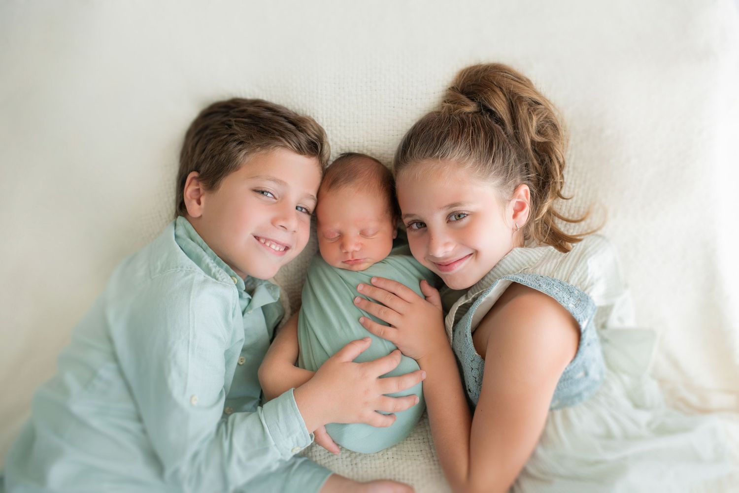 Family members in light blue clothing sharing intimate moment on white backdrop.