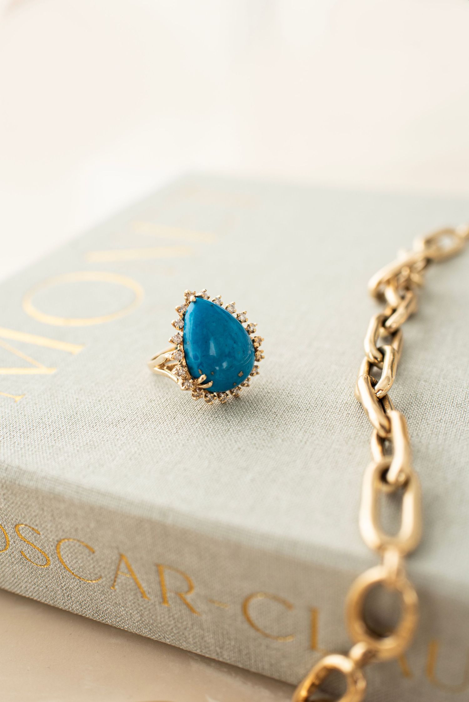 Close-up of turquoise gemstone set in gold jewelry piece on light background.