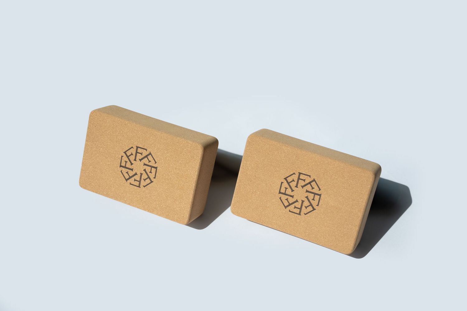 Two tan colored wooden blocks with circular designs cast shadows on a light surface.