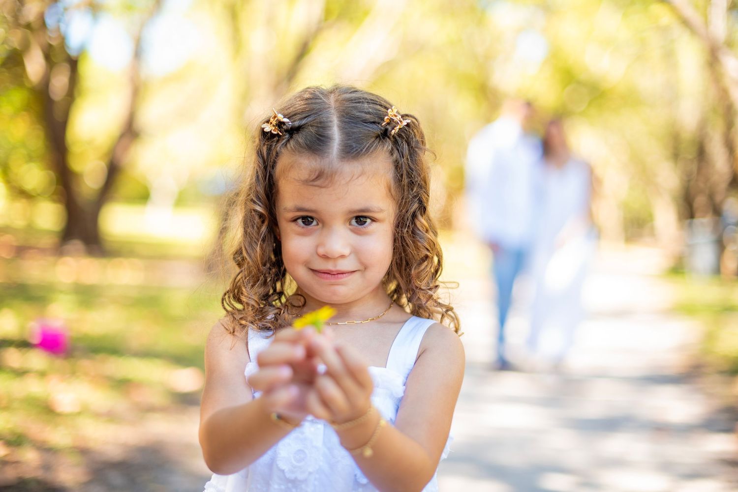 Young child with curly hair plays in a sunlit park on a warm autumn day.