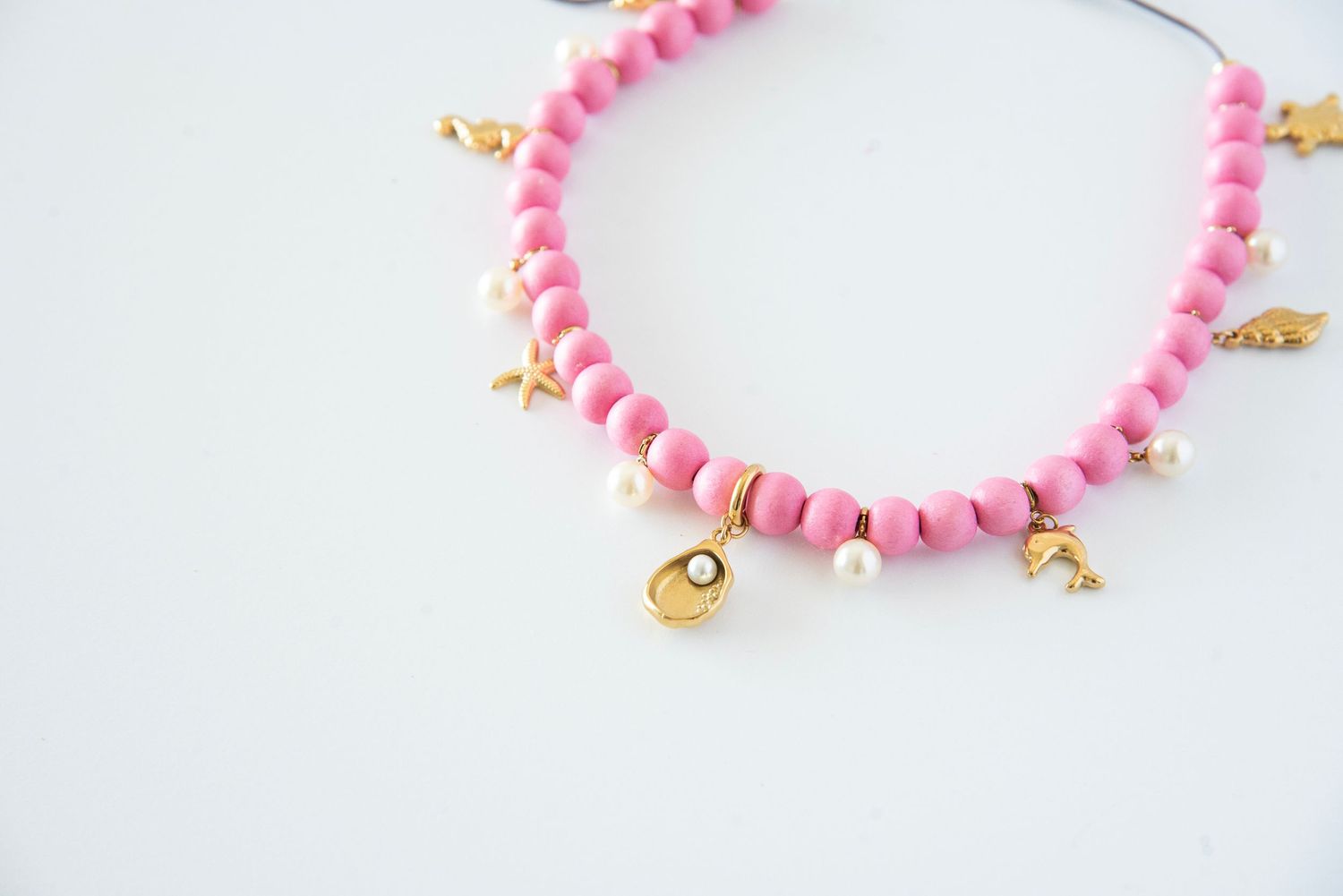 Pink wooden beaded bracelet with delicate gold charms laid flat on white background.