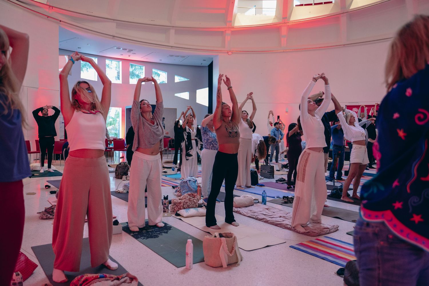 Group yoga class with participants raising arms overhead in a warmly lit circular studio during a wellness event.
