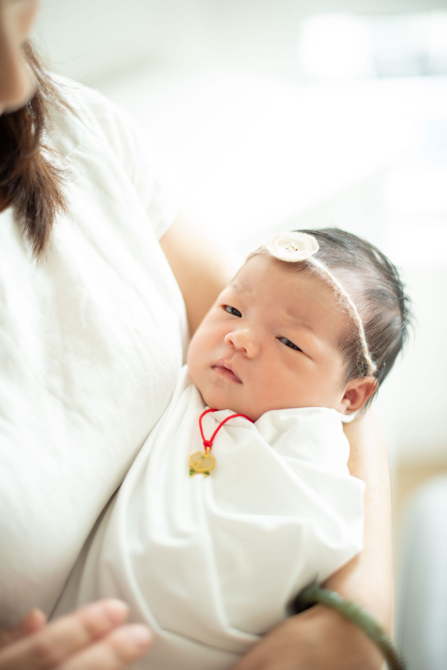 A baby lies peacefully on white bedding while being gently touched by a caregiver.