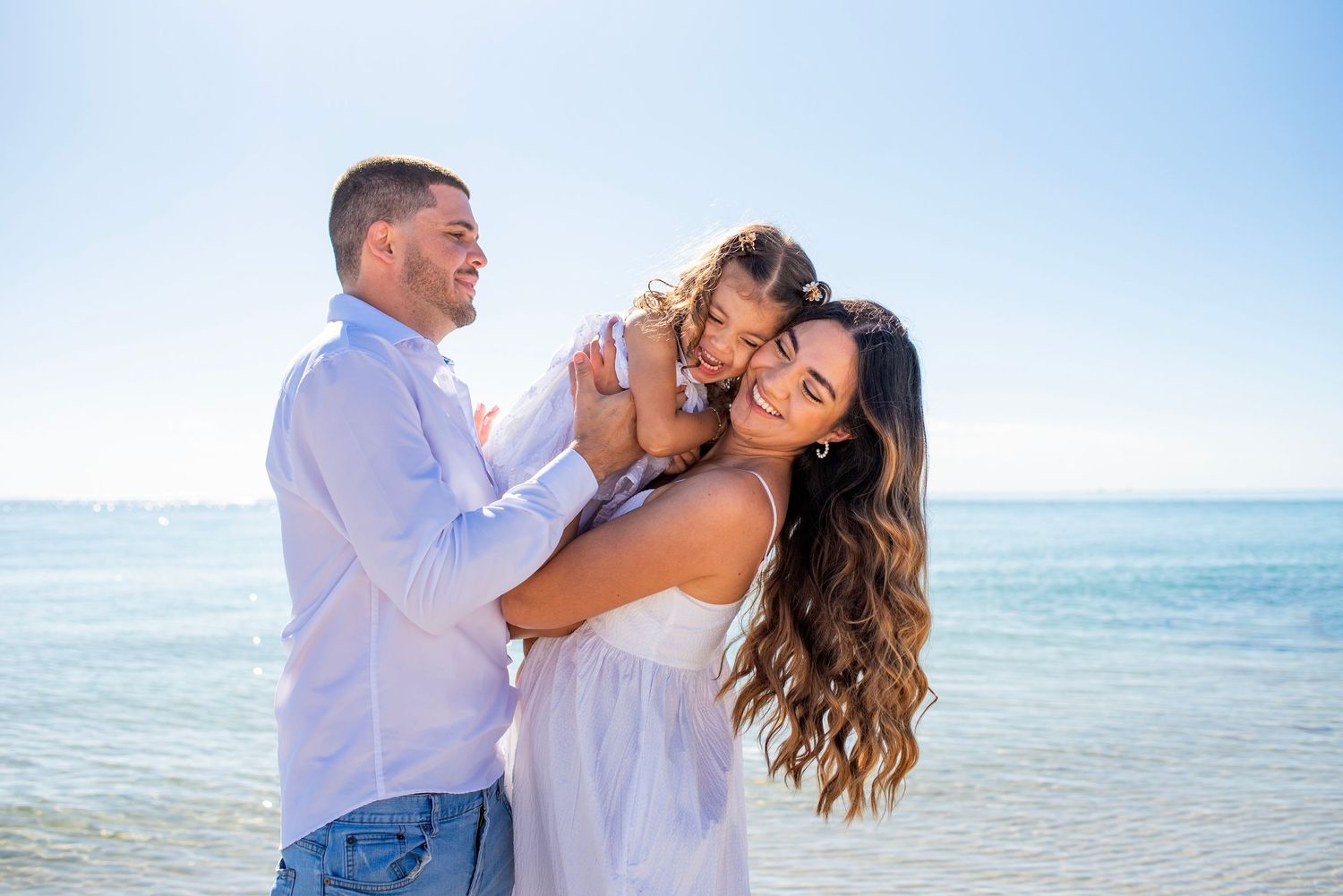 A couple embraces romantically on a tropical beach with turquoise ocean waters and blue sky in the background.