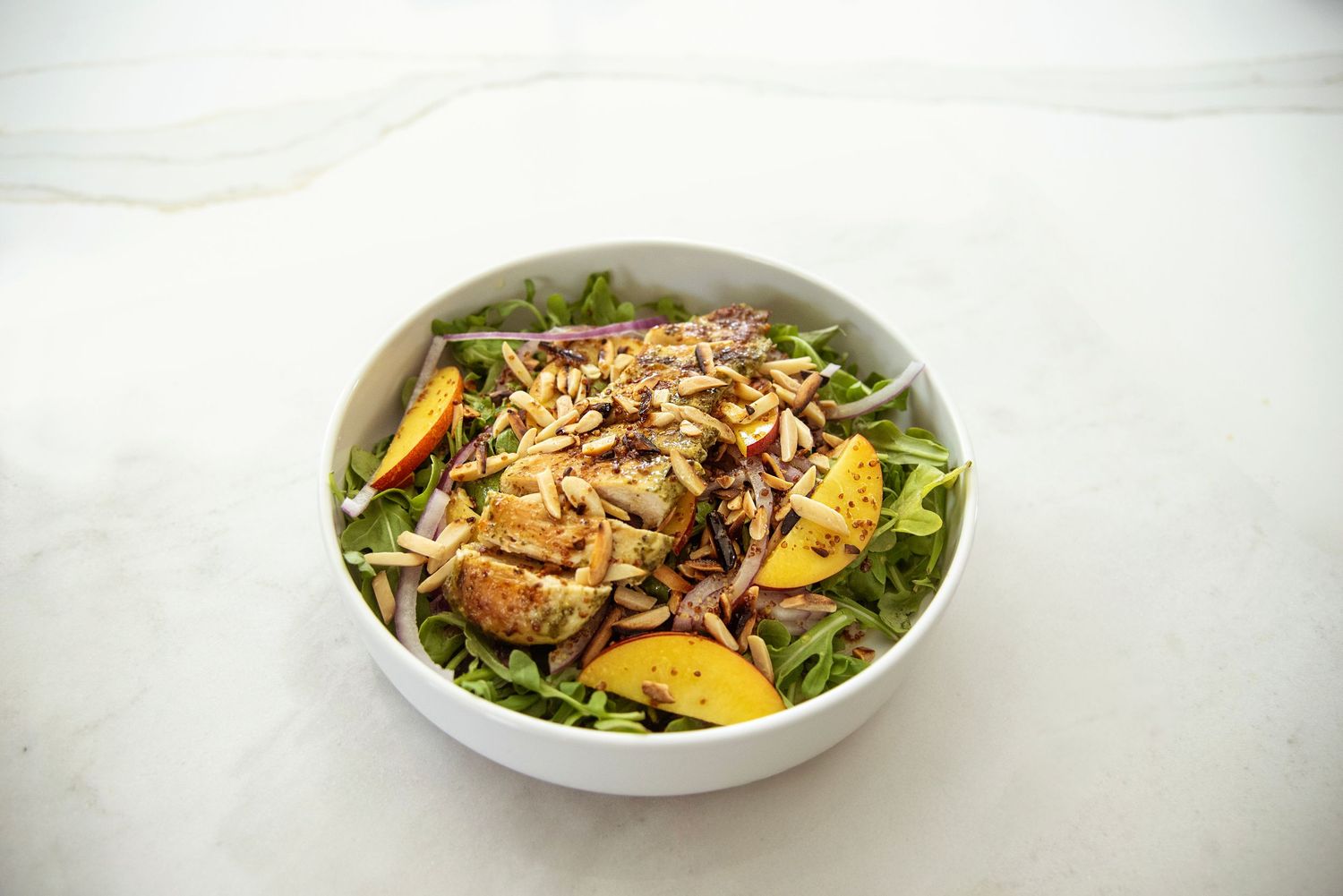 Fresh salad bowl with mixed greens and toppings on white marble surface.