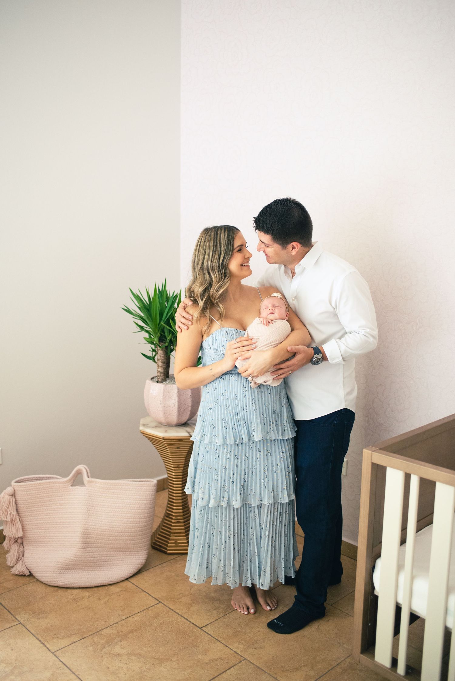 A couple in formal attire share romantic moments in a minimalist interior space with white walls and potted plants.