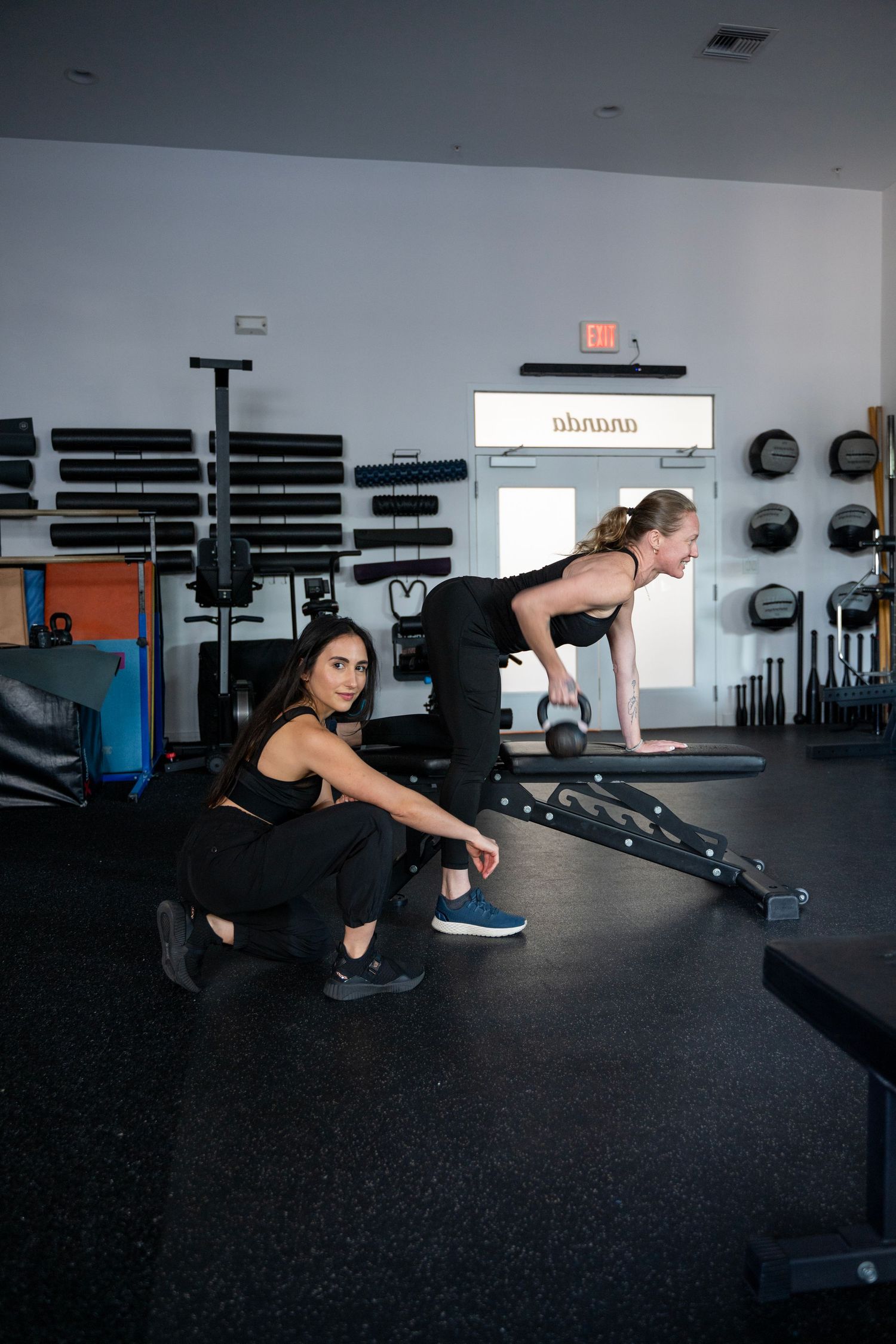 Person performing a series of bear crawl exercises on black gym floor with weight racks in background.
