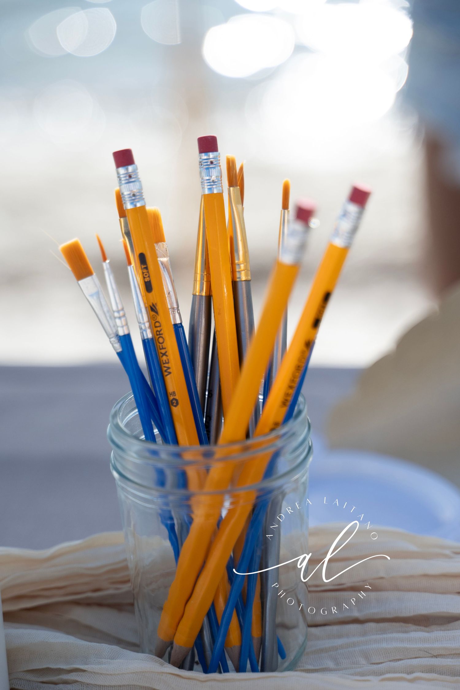 Yellow and blue pencils stand upright in a clear glass jar against a soft bokeh background.
