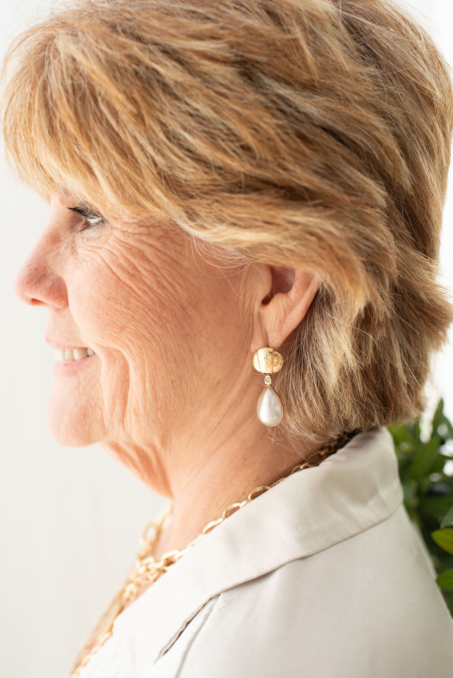 Side profile portrait showing gold earrings and necklaces against white background.