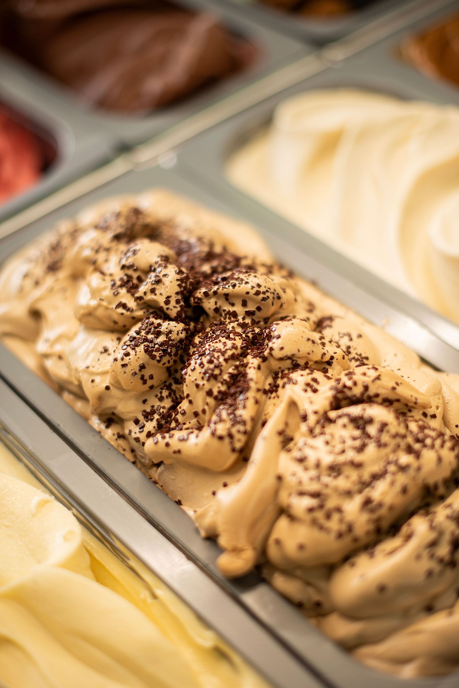 Creamy gelato with chocolate sprinkles displayed in a metal tray at an Italian ice cream shop.