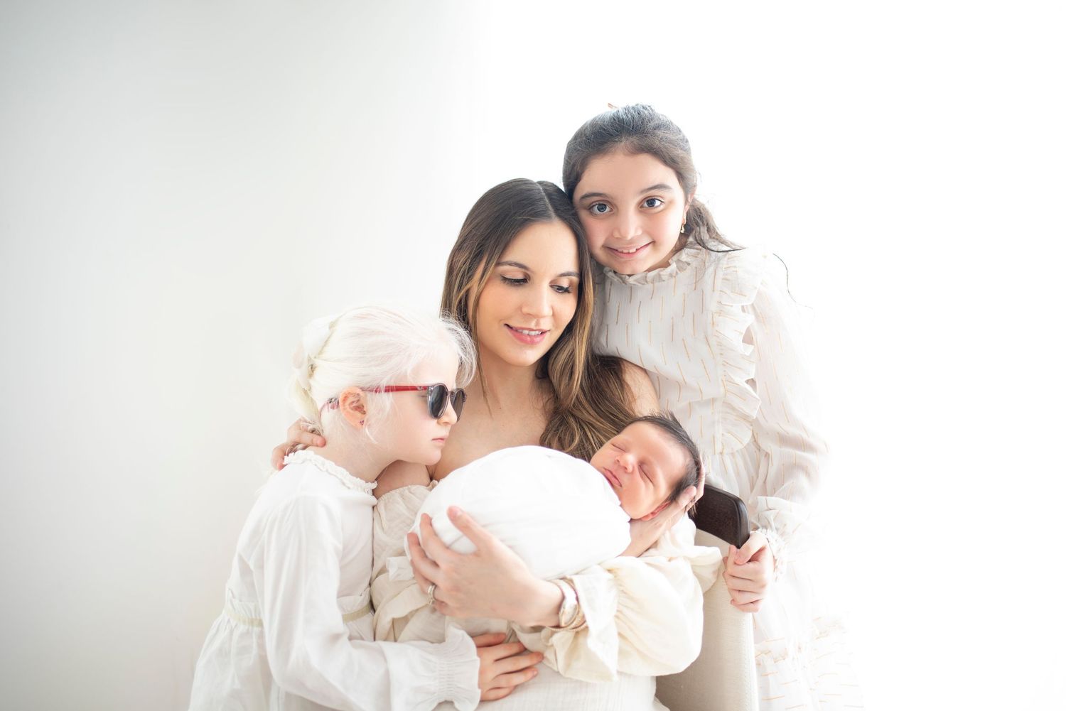 Family members embrace while wearing coordinated white outfits in studio setting.