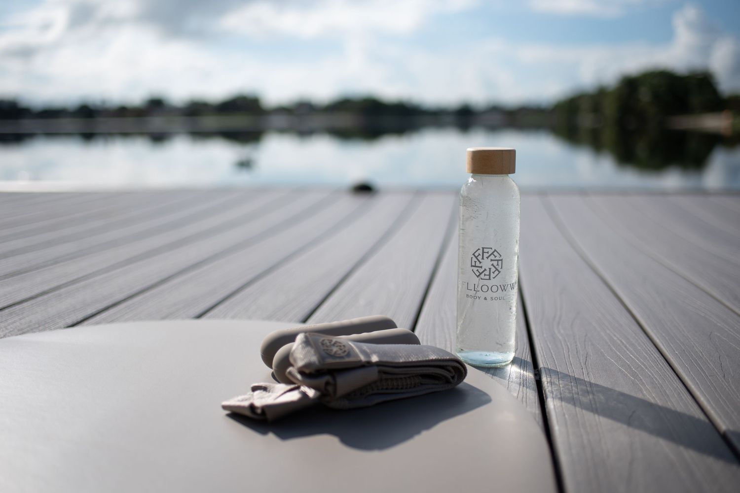 Yoga props and water bottles arranged on wooden dock by lake.