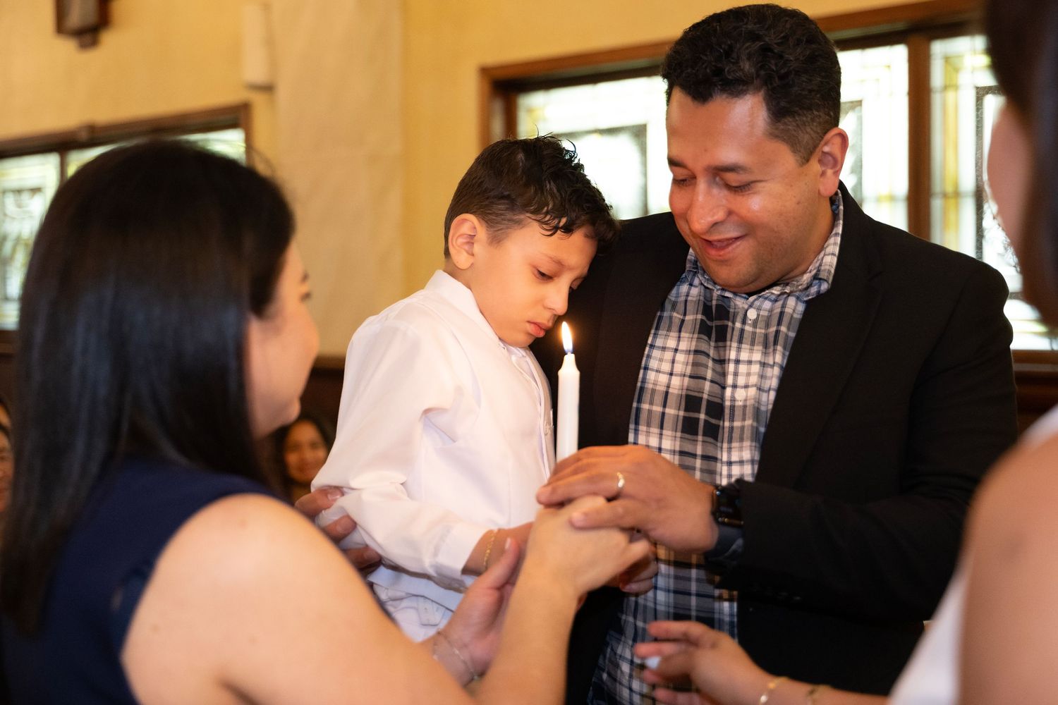 Father holding young boy during First Communion ceremony in church, lighting a candle.