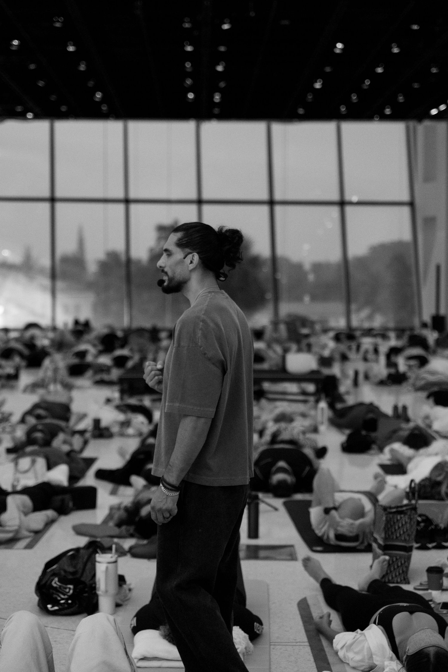 Black and white photo of a yoga instructor walking among students lying on mats in a large modern studio.