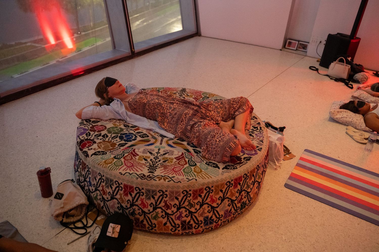 Person resting on a large round floral bean bag chair in a modern room with colorful rug and red ambient lighting.