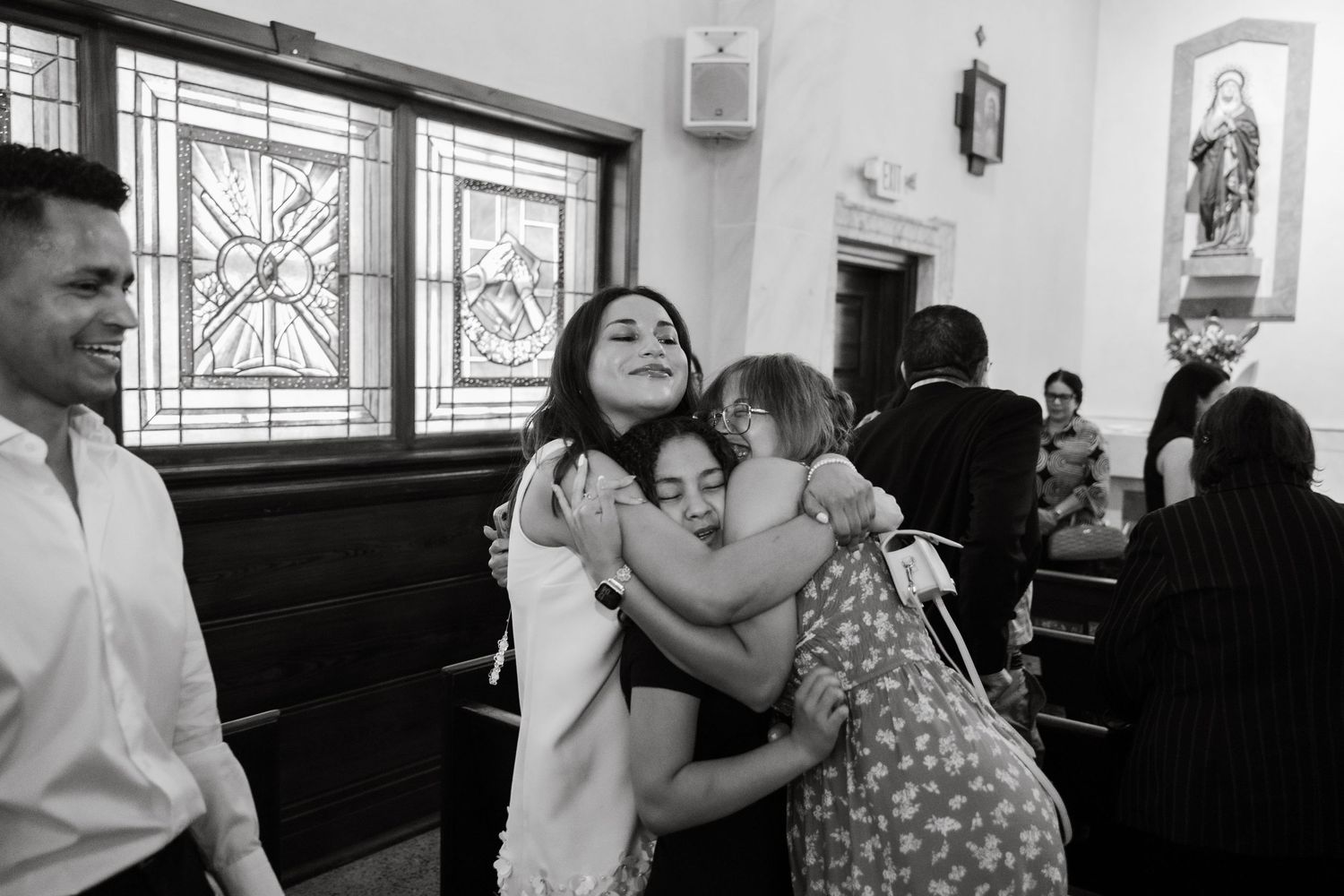 Black and white photo of people sharing warm hugs inside a church during a special ceremony.