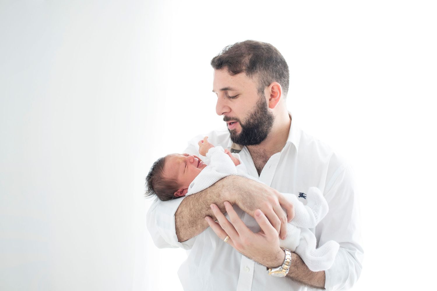 Father in white shirt tenderly holds newborn baby during photo session.