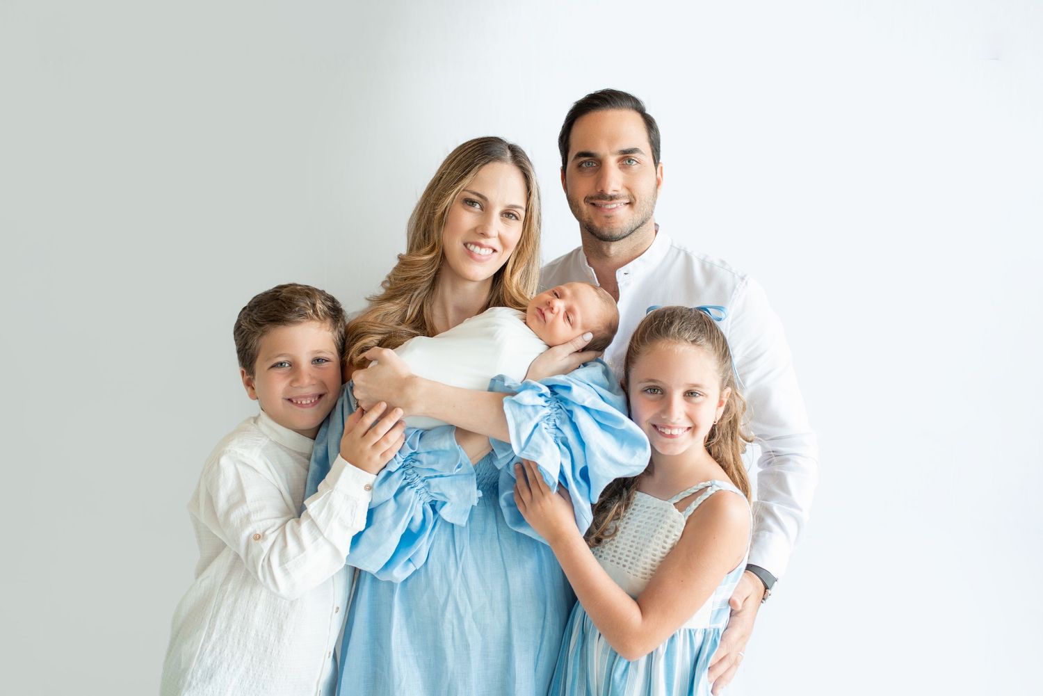 Family wearing coordinated white and light blue outfits poses together for a professional portrait session.