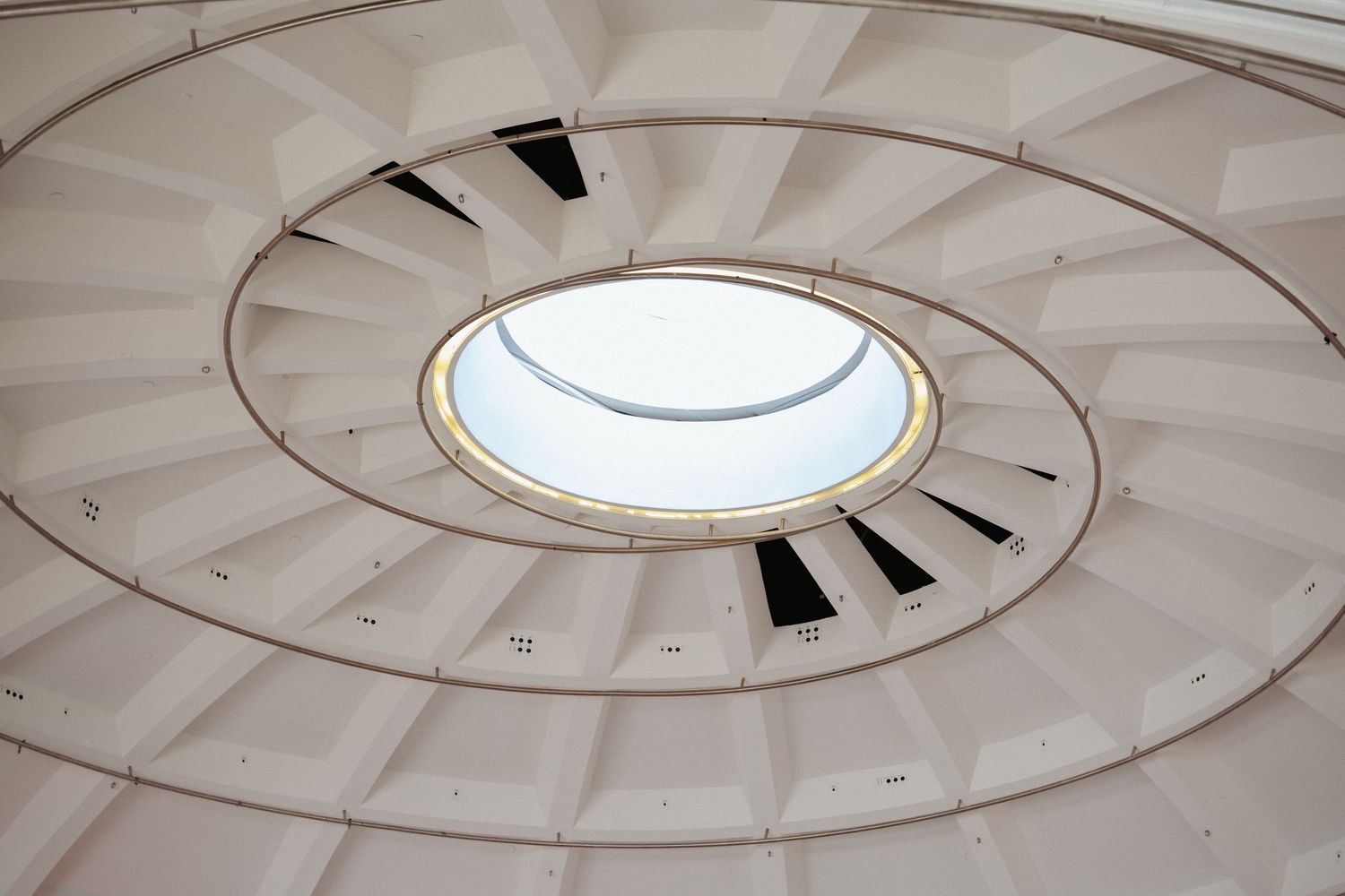 Architectural spiral ceiling with circular skylight, white geometric panels radiating outward in modern interior design.