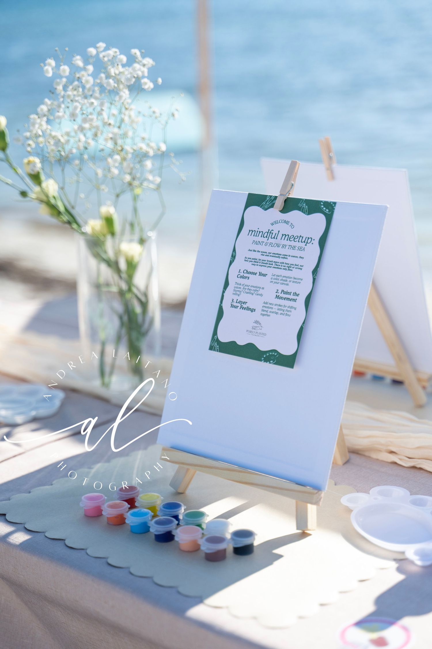 A wedding menu card on an easel with watercolor paints and baby's breath flowers in a vase against a blue background.