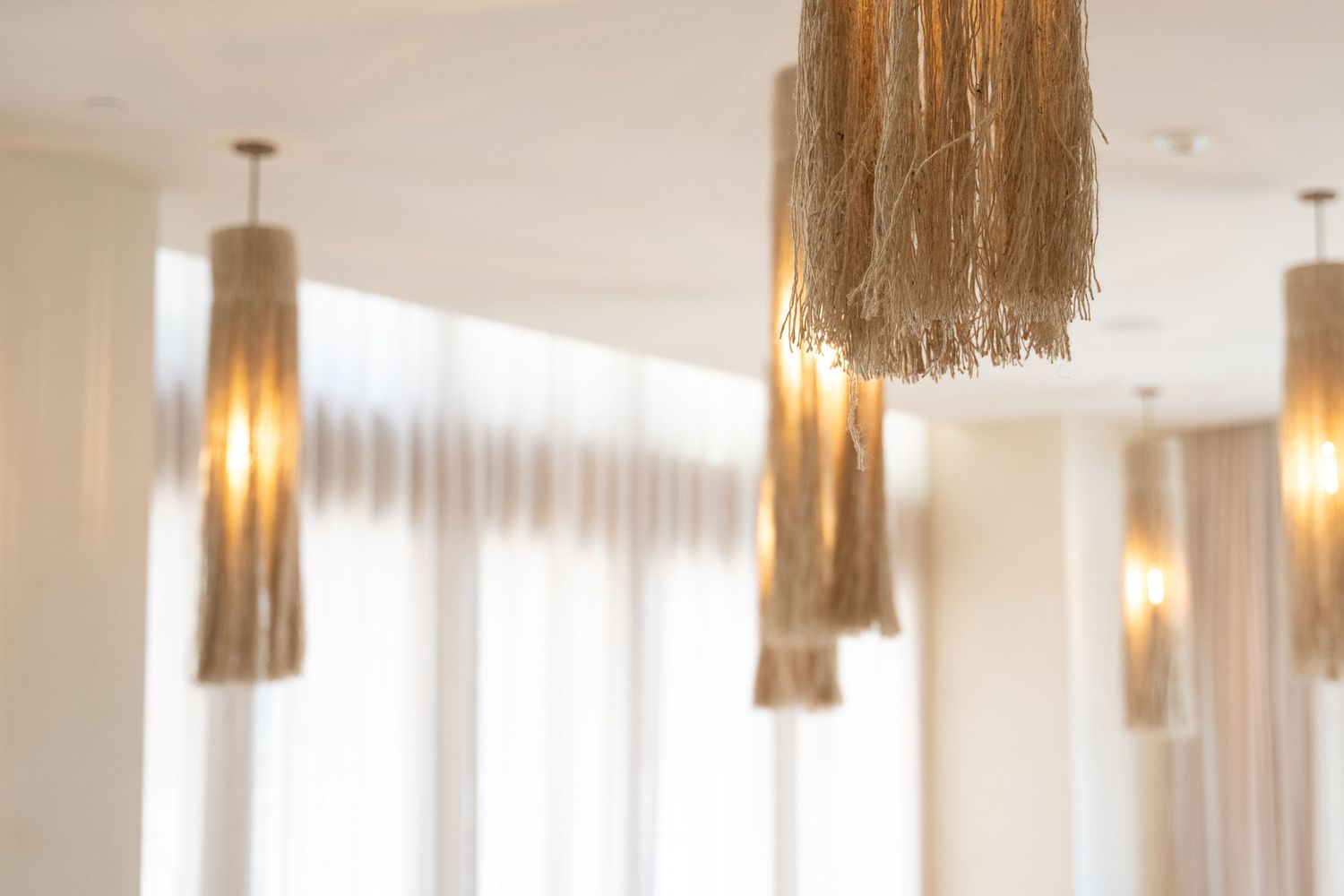 Elegant hanging pendant lights with natural fiber fringe shades in a bright modern interior space.