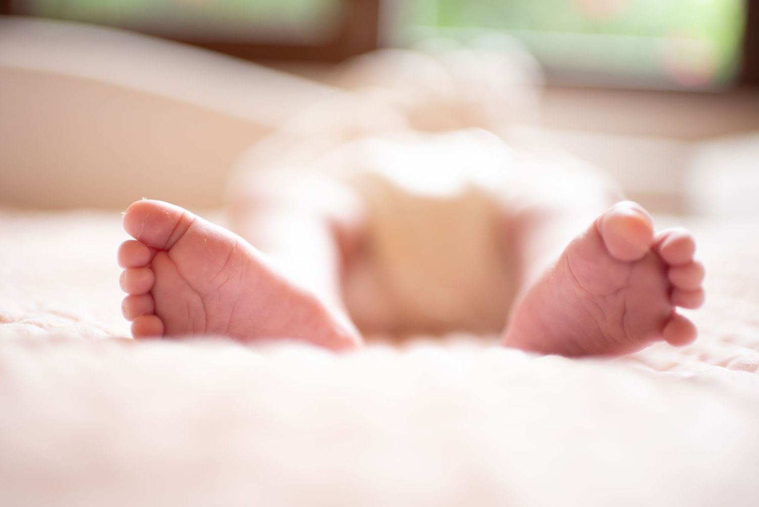 A row of tiny newborn baby feet lined up in a soft, warm light creating a tender nursery scene.