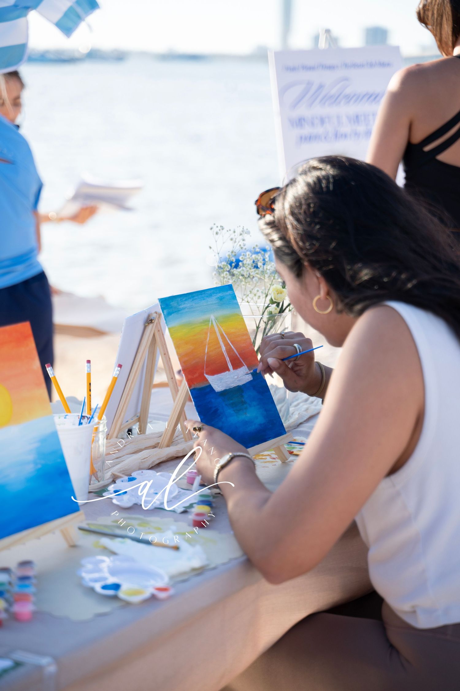 Person working on watercolor painting at a table with art supplies and papers spread out during creative session.