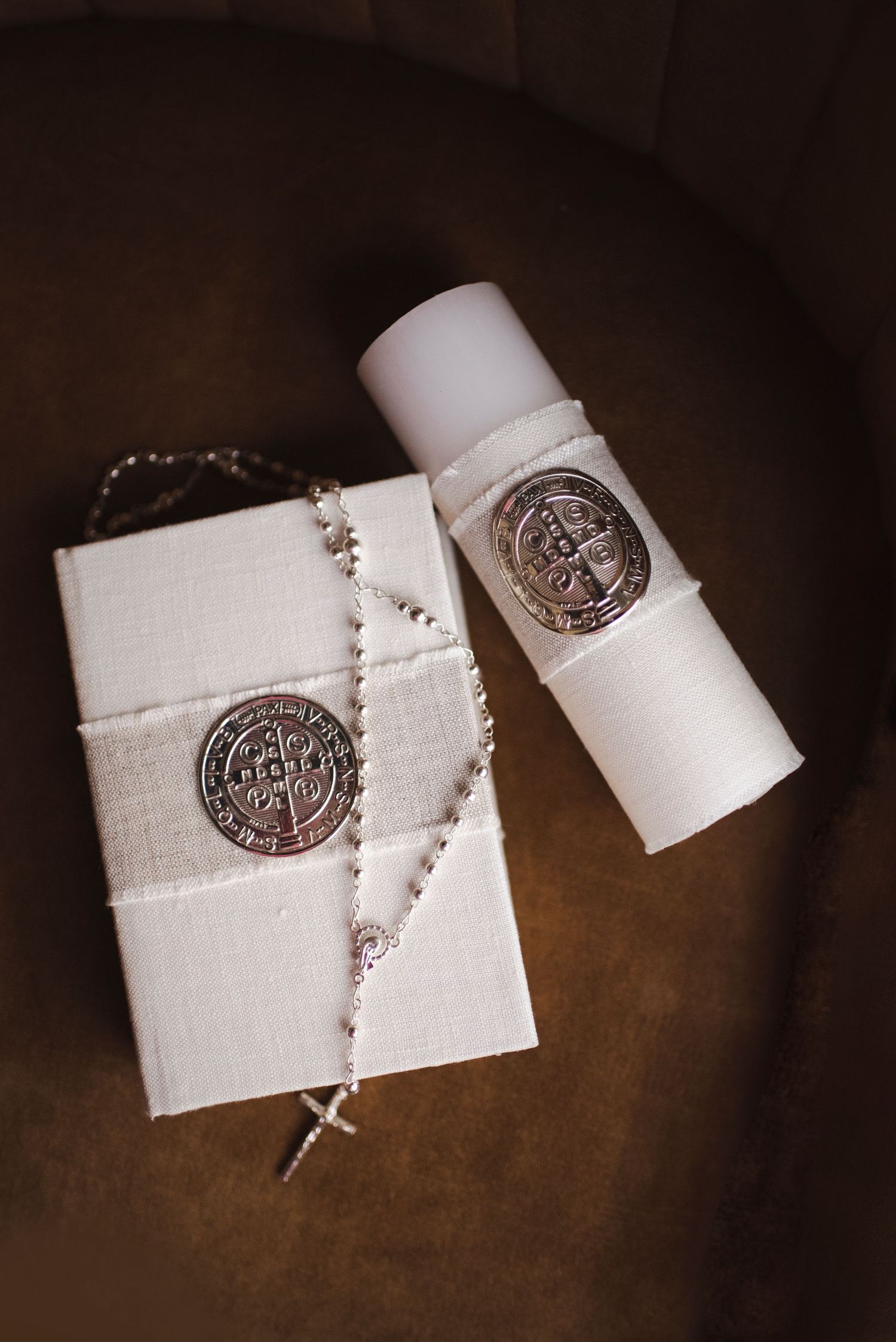 White rosary beads and religious medallions arranged on dark brown surface.
