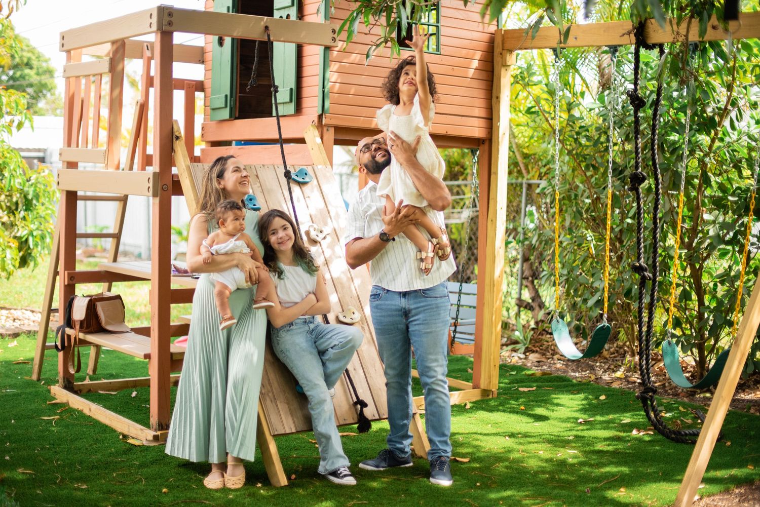 A group enjoys a fun moment together by a wooden backyard playset with swings on a sunny day.