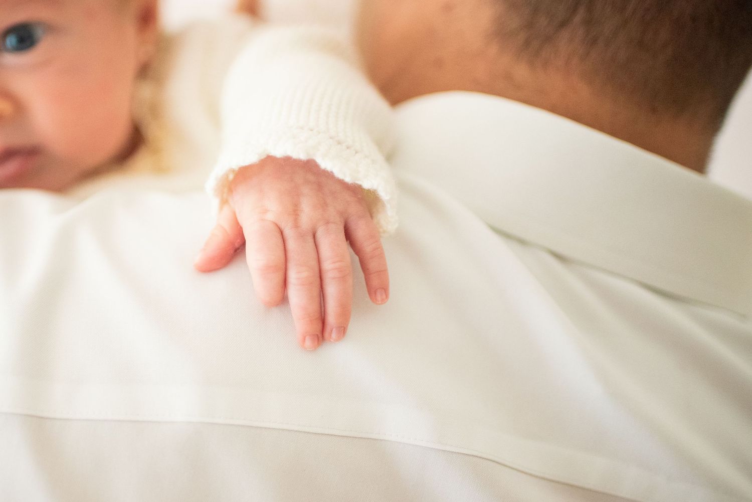 Close-up view of hands gently holding a sleeping newborn baby wrapped in soft white blankets.