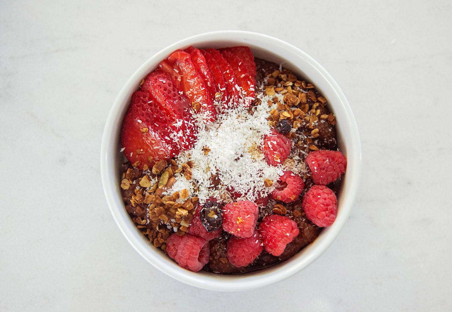 Fresh red raspberries with white powdered sugar topping in white ceramic bowl.