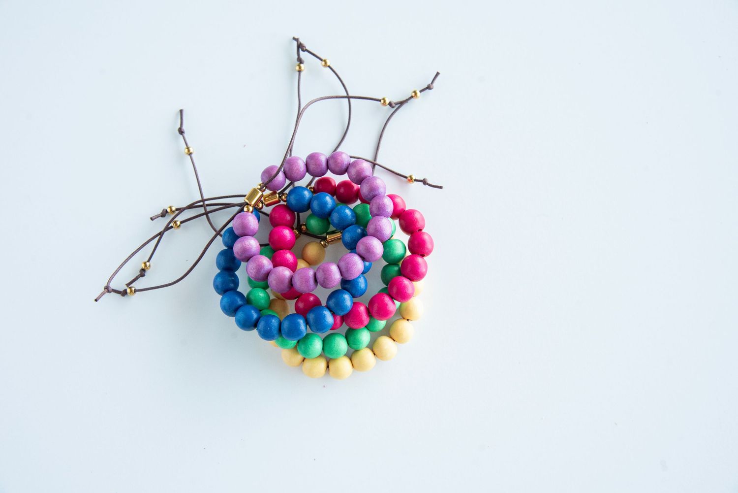 Rainbow colored wooden bead necklaces arranged on tree branch against white background.