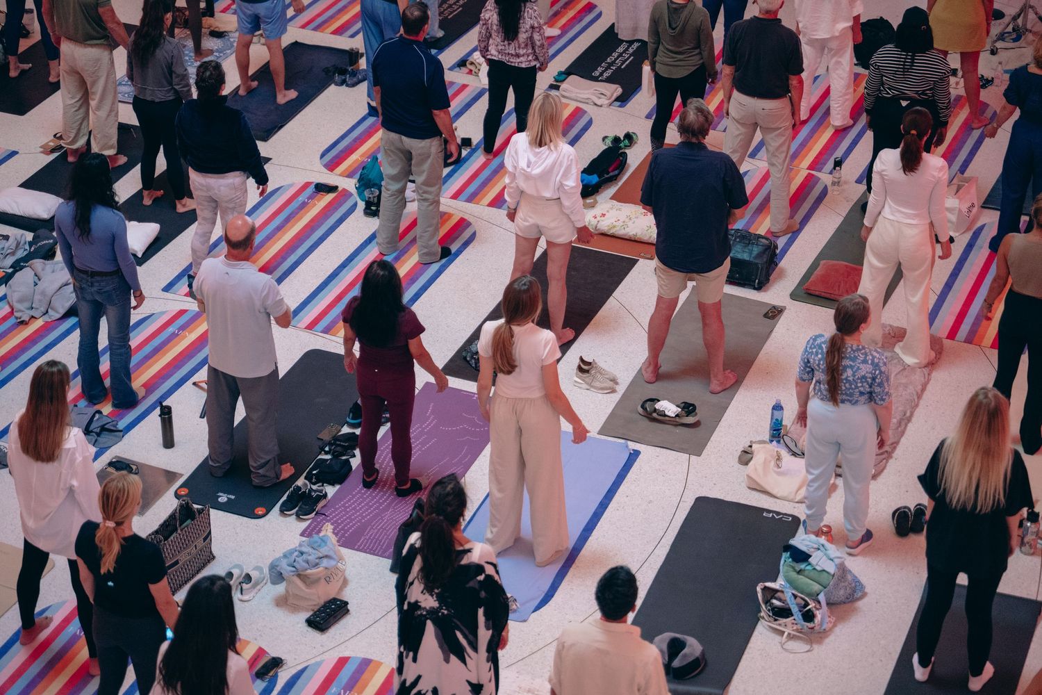 Aerial view of a large group yoga class on colorful striped mats in a bright open space.