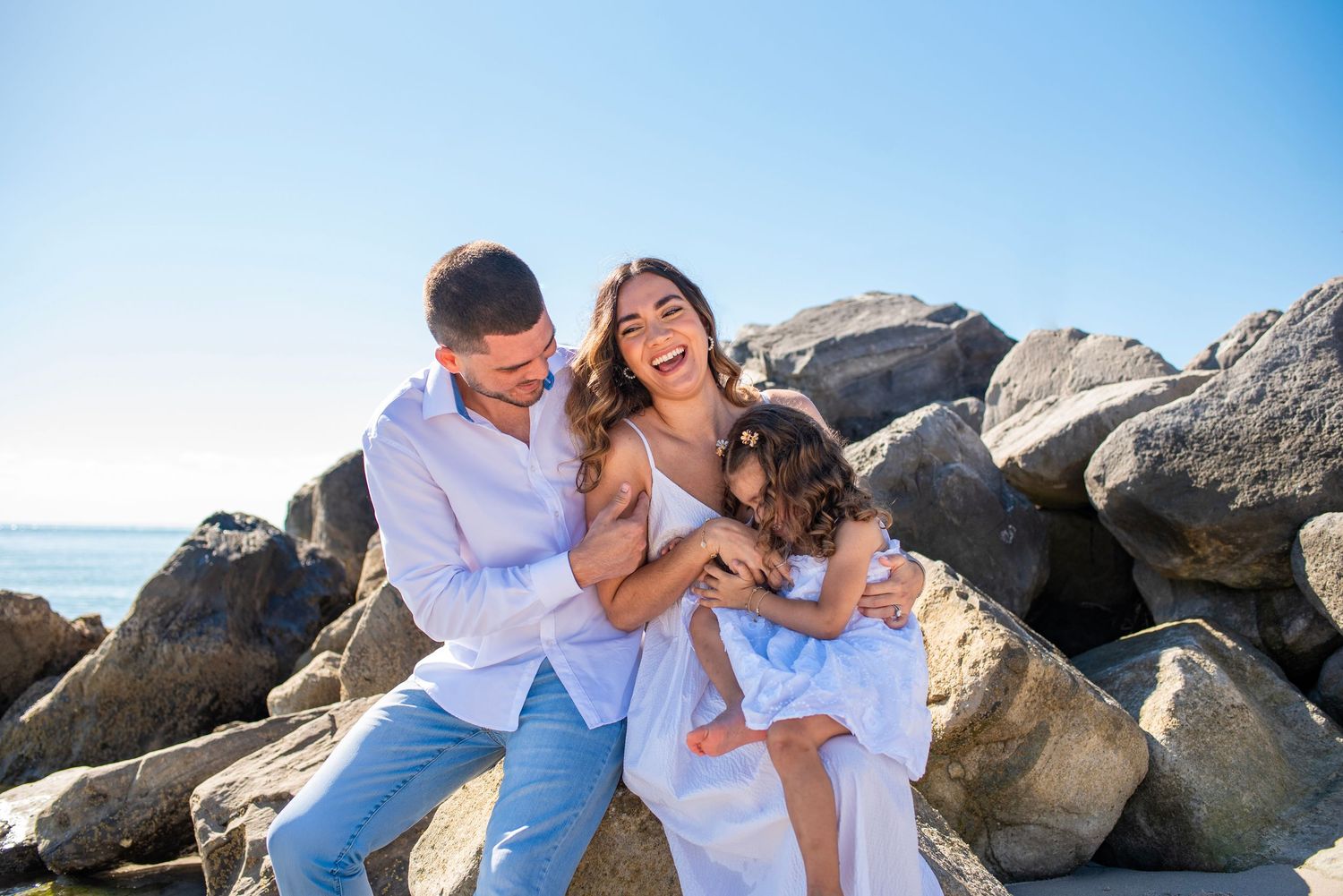 A joyful family moment with a dog among coastal rocks by the ocean on a bright sunny day.