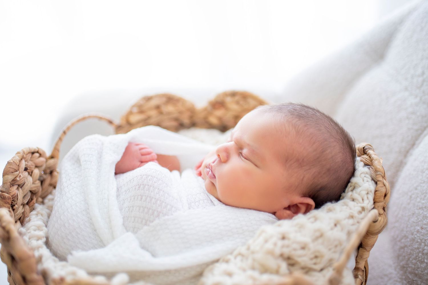 Sleeping newborn baby wrapped in white blanket lying on soft textured beige blanket.