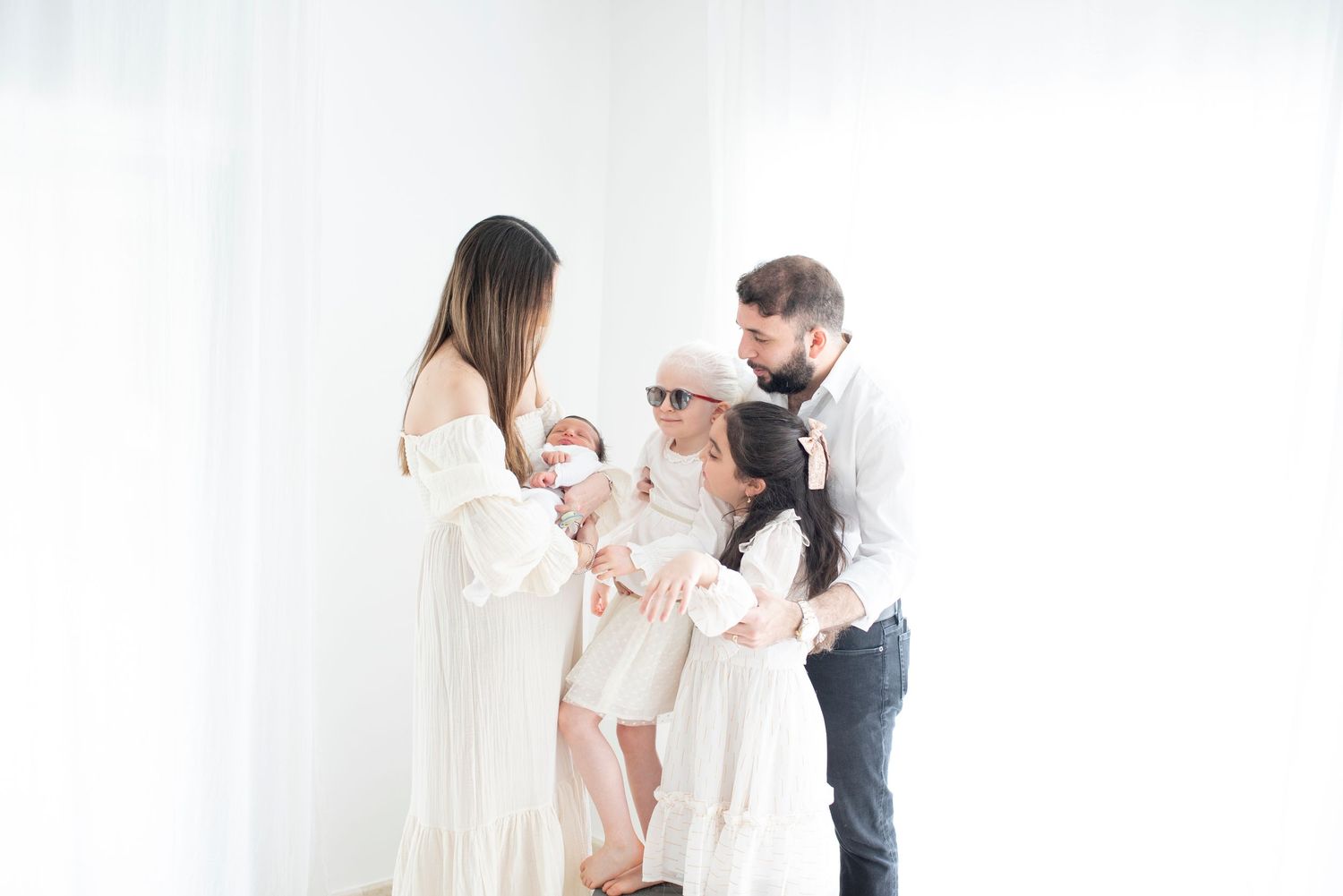 Intimate family portrait in white clothing against bright minimalist background.